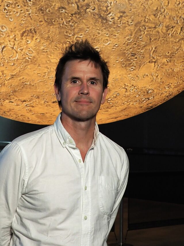 Artist Luke Jerram, wearing a white button down shirt, is pictured standing in front of his artwork Mars.