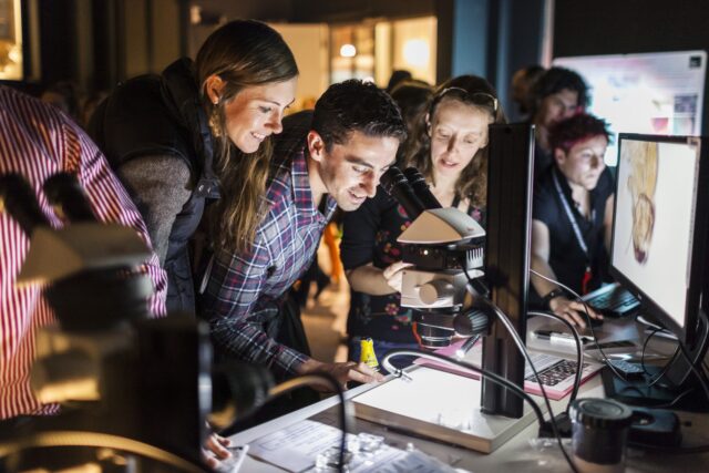 A group crows around a microscope at a Science Museum Lates event.