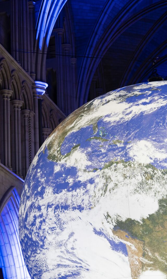 Gaia by Luke Jerram is pictured suspended inside Southwark Cathedral, which is dark apart from some carefully positioned blue uplights that illuminate the Cathedral's dramatic architecture. Gaia is a large recreation of Earth, created to scale using NASA data and imagery.