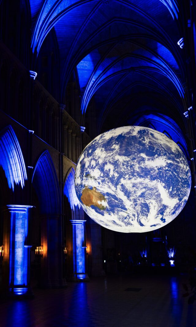 Gaia by Luke Jerram is pictured suspended inside Southwark Cathedral, which is dark apart from some carefully positioned blue uplights that illuminate the Cathedral's dramatic architecture. Gaia is a large recreation of Earth, created to scale using NASA data and imagery.